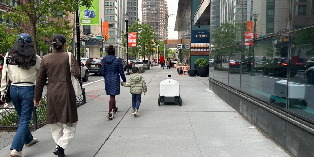 A delivery robot shares a sidewalk with pedestrians in Jersey City, New Jersey.
